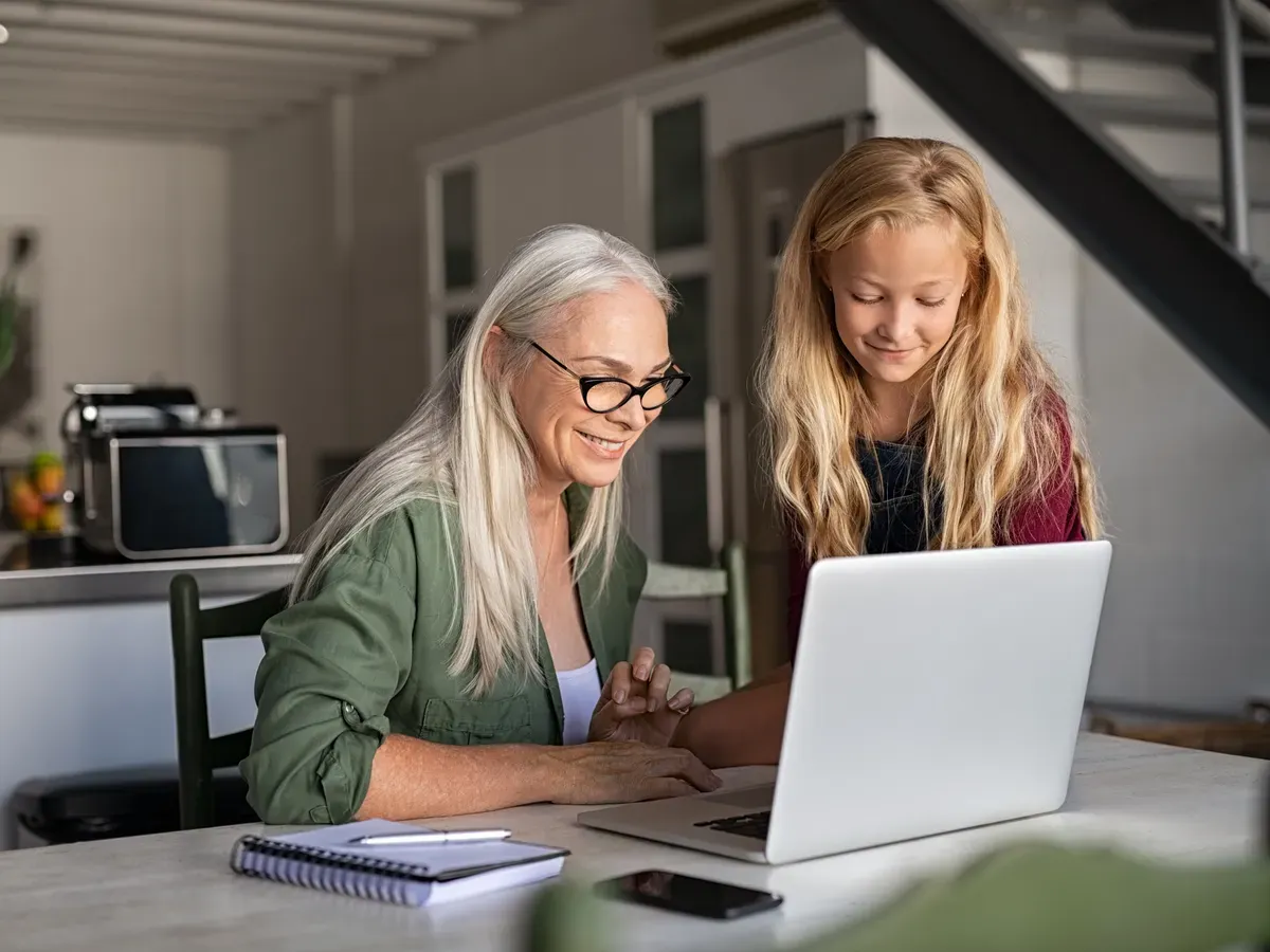 Two people sit side by side at the kitchen table, joining a video appointment on the same laptop