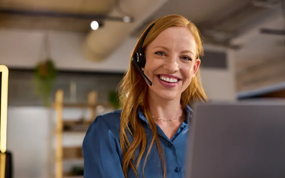 A person wearing a headset smiles while taking a call at a desk