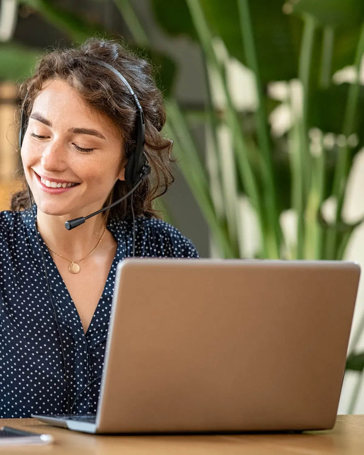 A clinician wearing a headset makes notes at a laptop during a video appointment