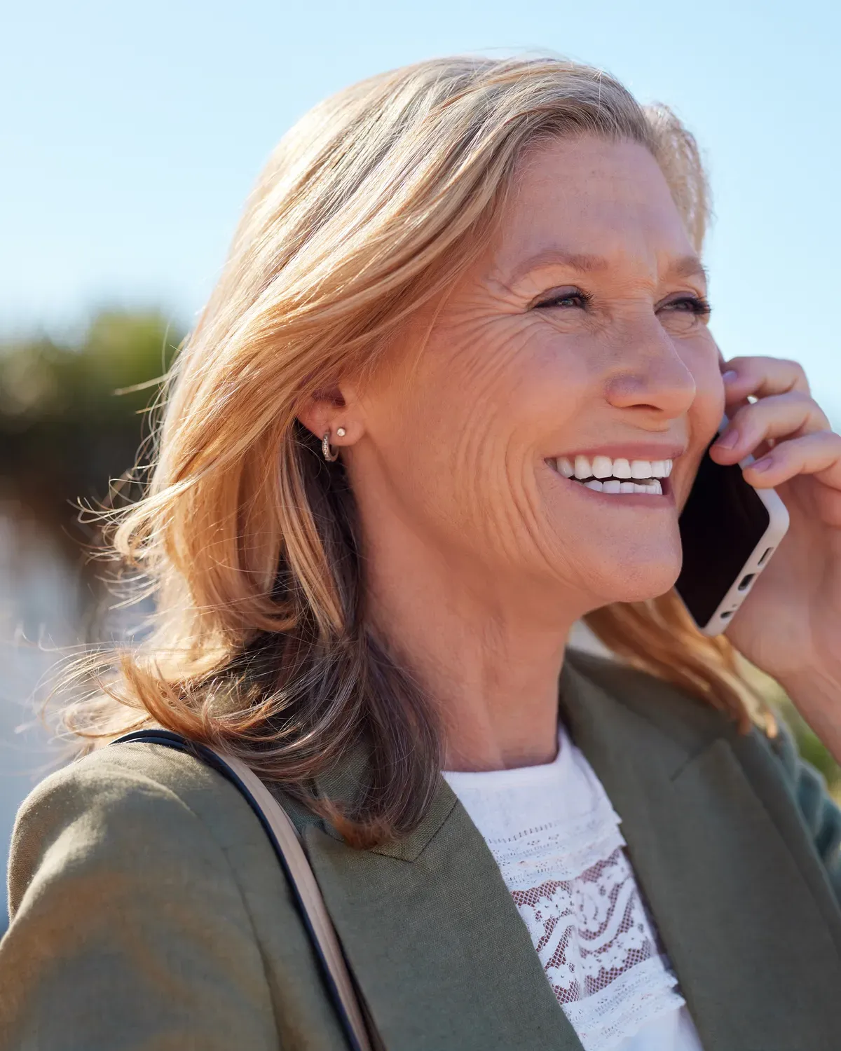 A woman stands outside in the sun, talking on her phone