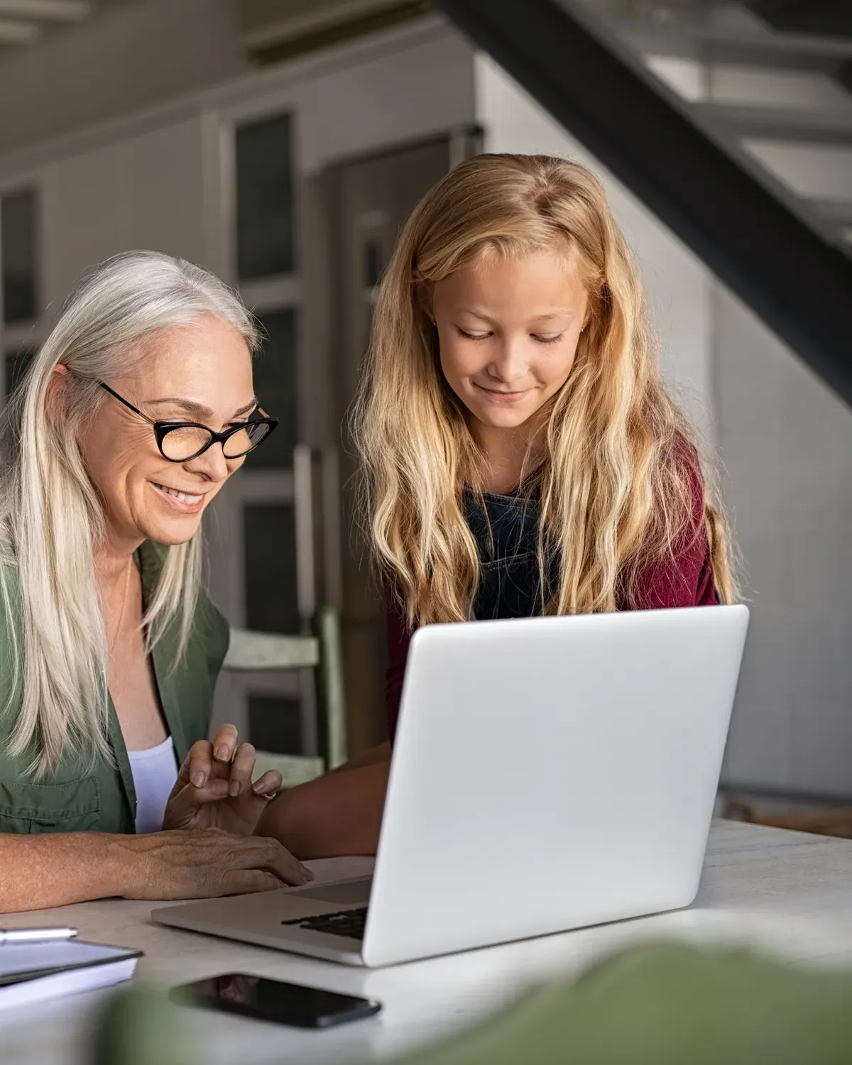 Two people sit side by side at the kitchen table, joining a video appointment on the same laptop